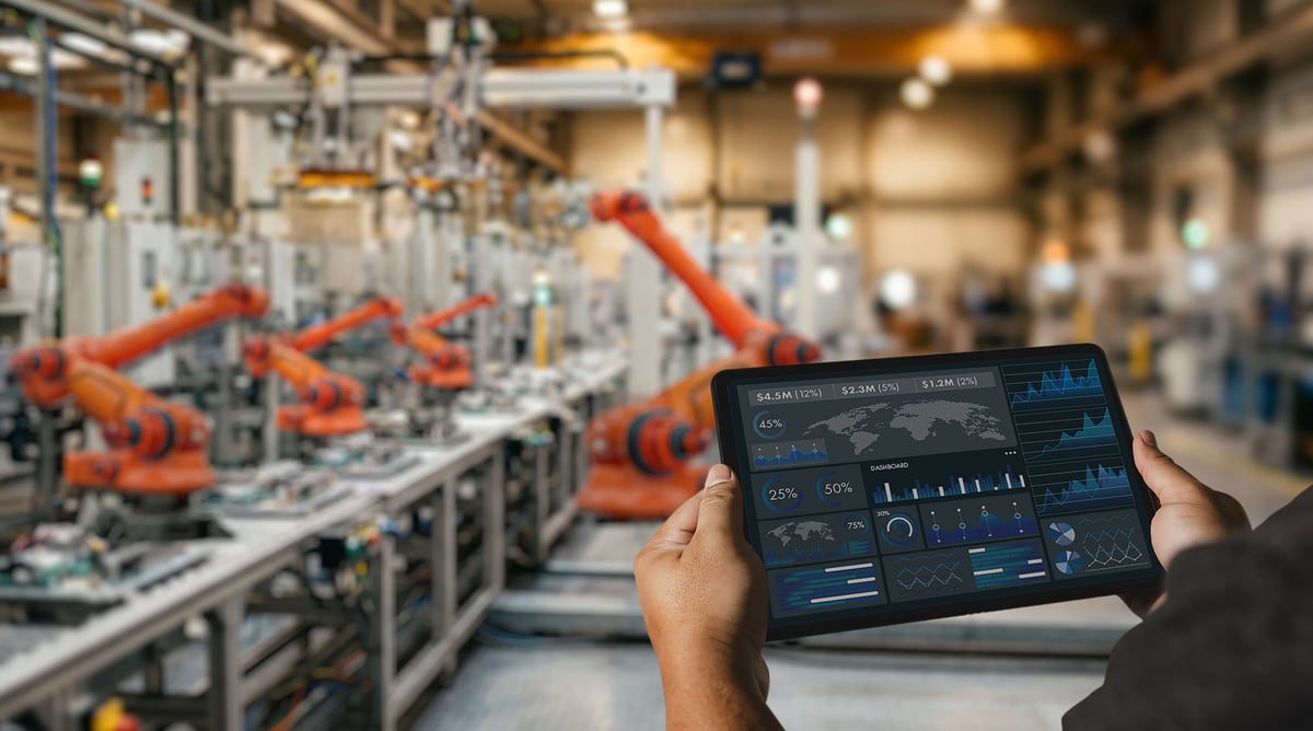 Engineer holding a tablet showing operational performance dashboards in front of a production line
