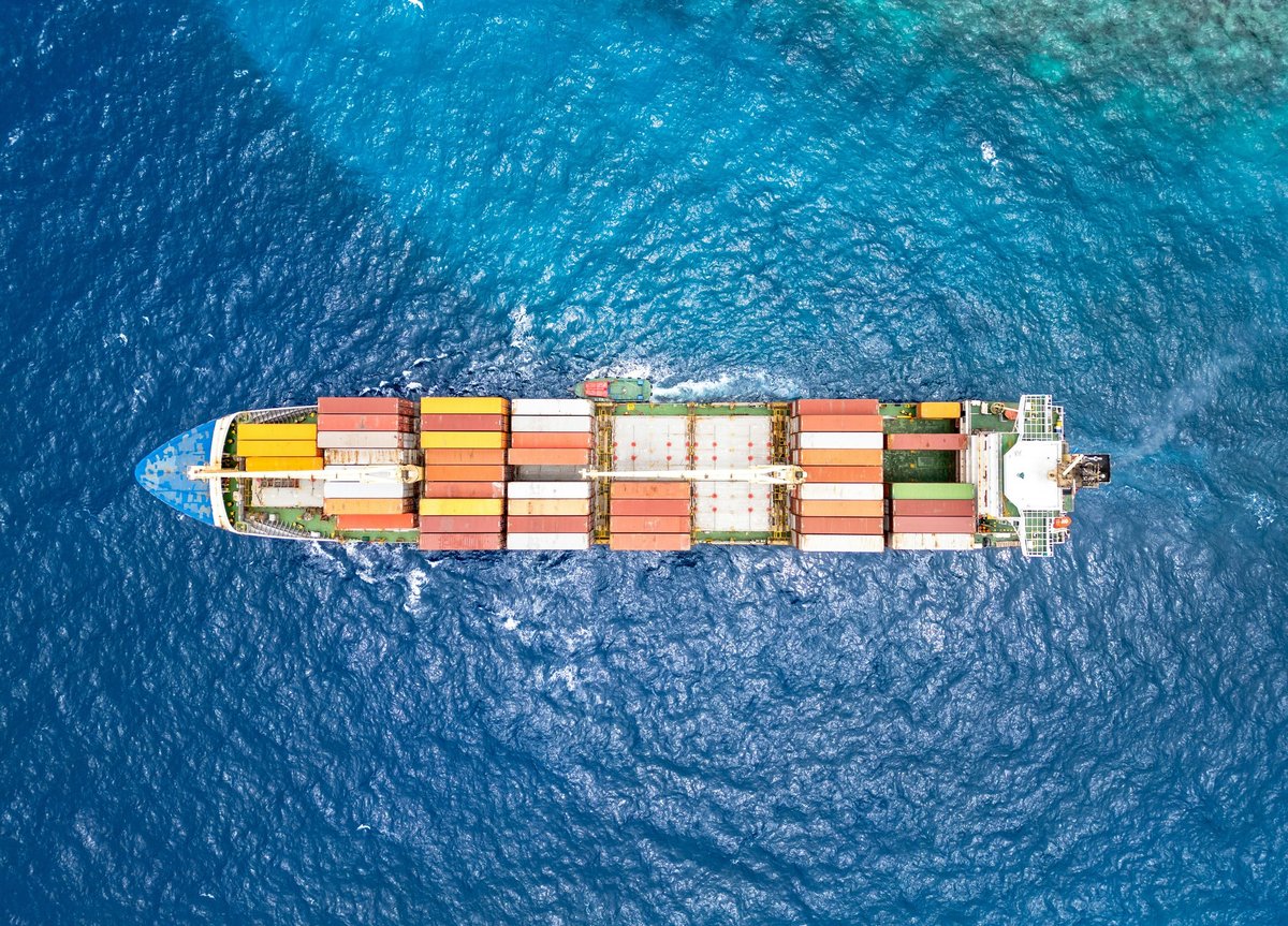 Overhead view of a container ship carrying multicoloured freight containers across blue water